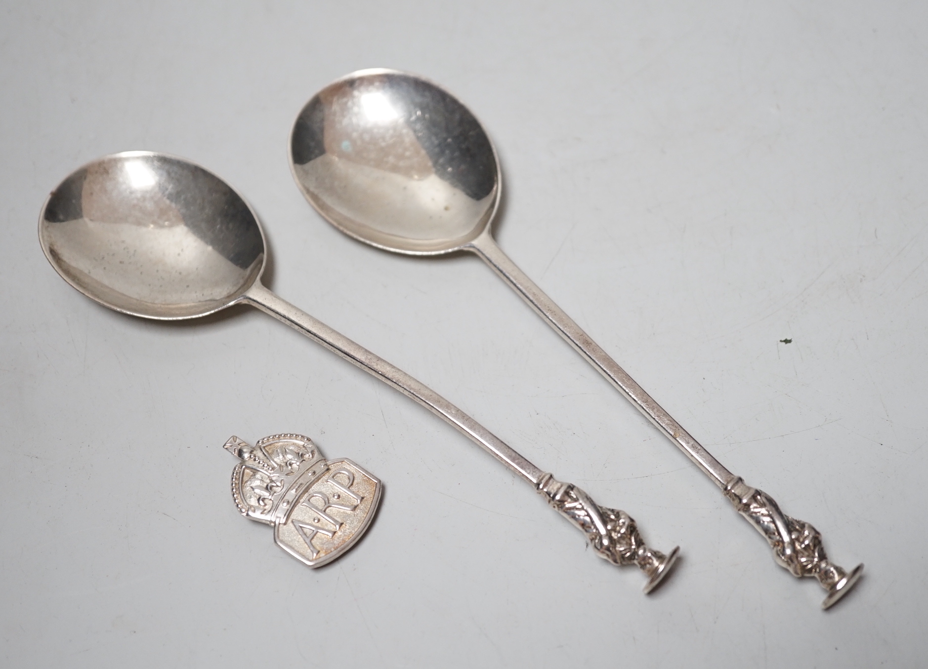 A pair of Edwardian silver apostle spoons, London, 1906 and an ARP badge